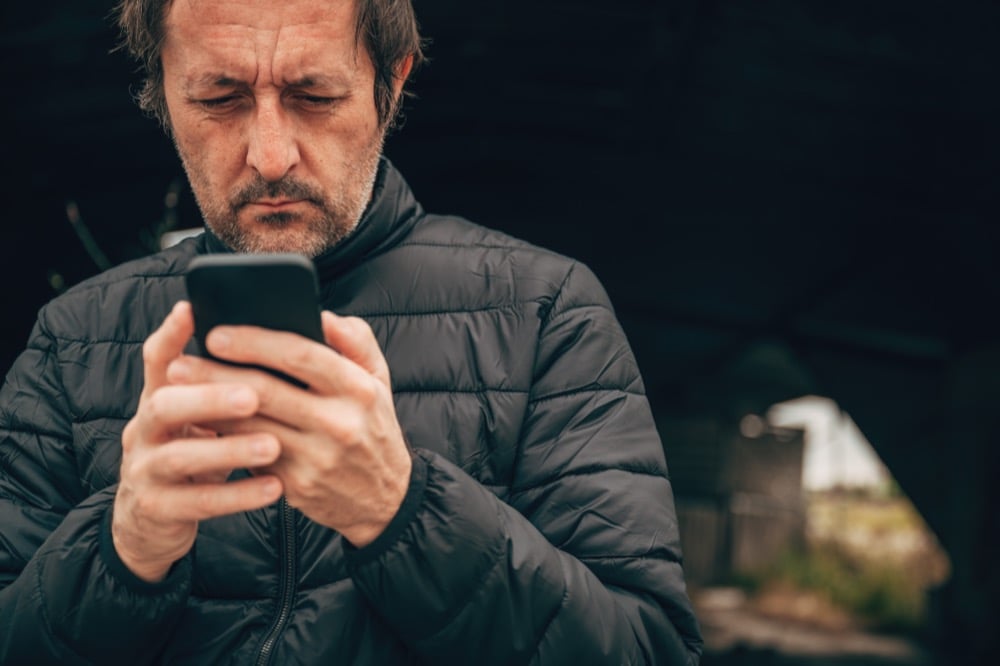 A man in a black puffer jacket looking at his smartphone outdoors