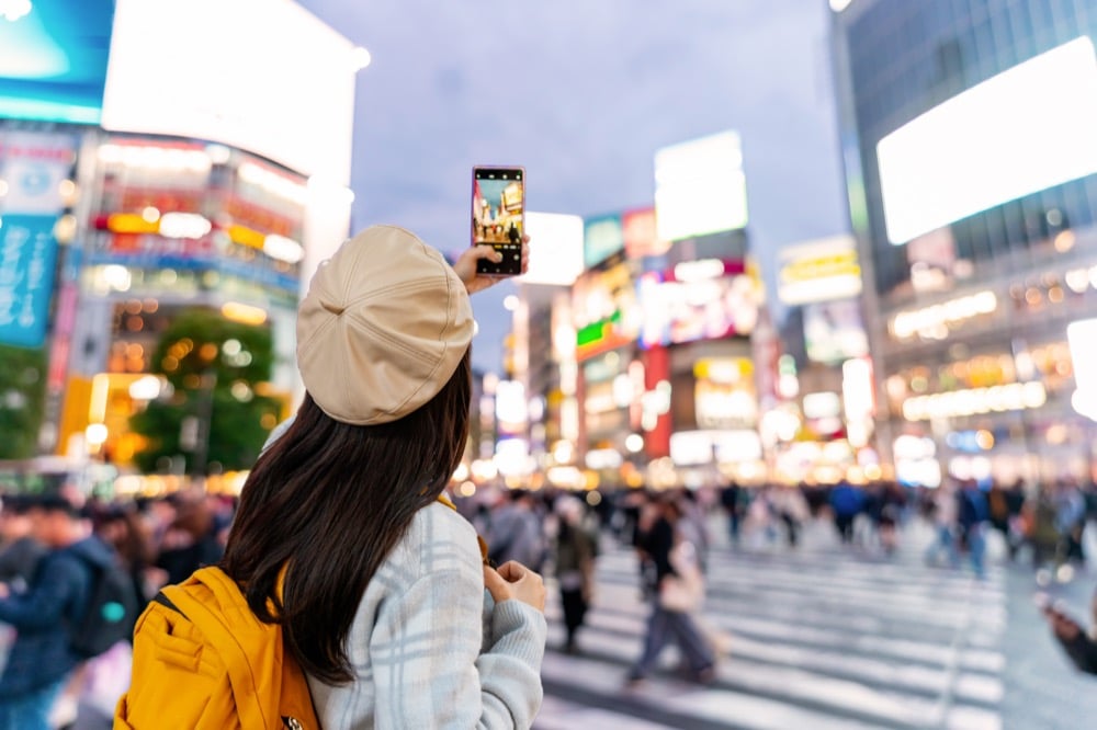 A woman photographing Shibuya Crossing at night with her smartphone