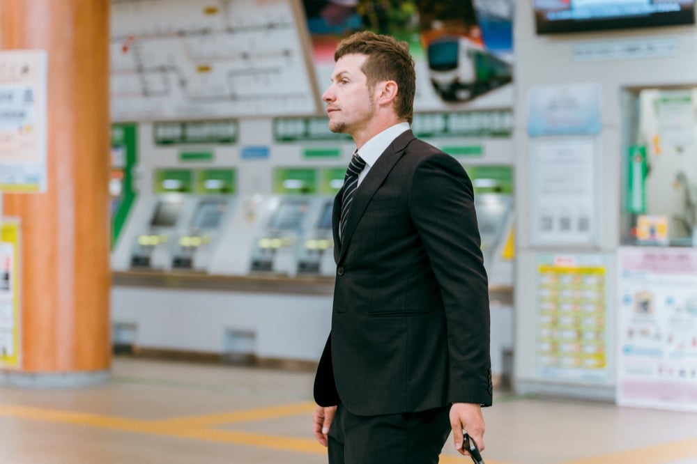 A businessman standing in a Japanese train station near ticket machines