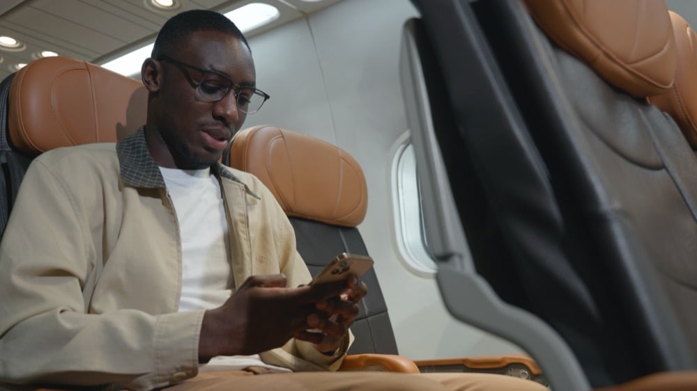 A man wearing glasses sitting in an airplane seat and looking at his smartphone