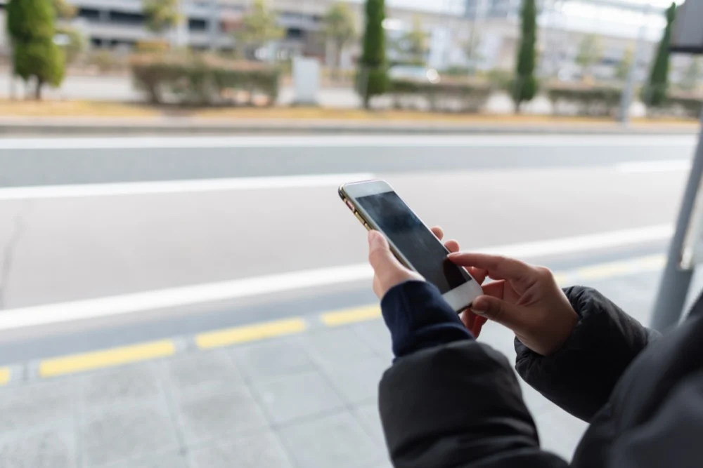 A close-up of a person's hands using a smartphone by the side of a road outdoors