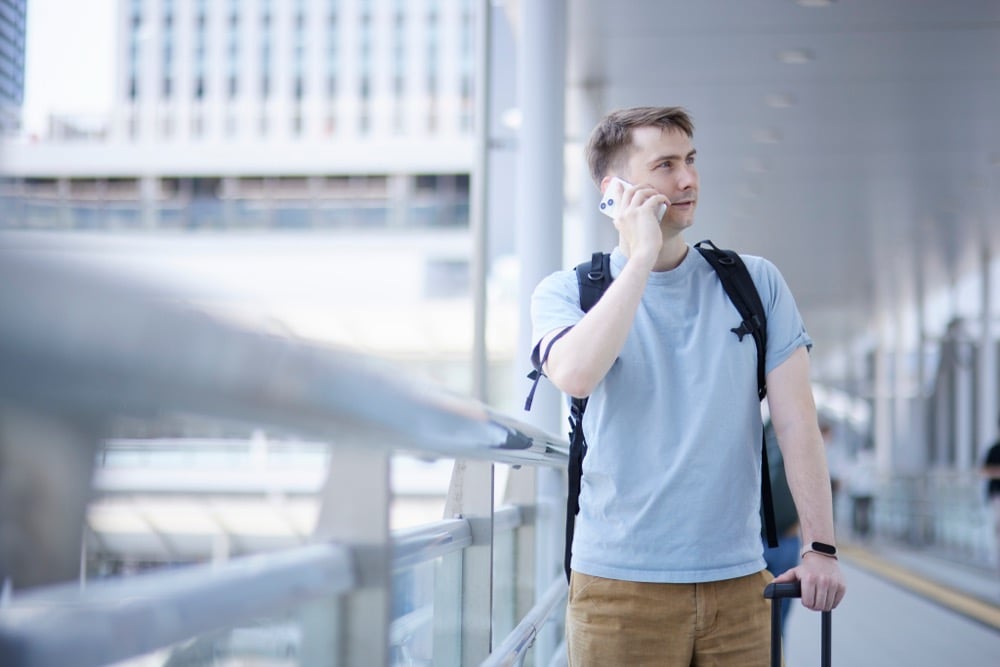 A foreign traveler making a phone call with a suitcase at a Japanese train station using Mobile Suica