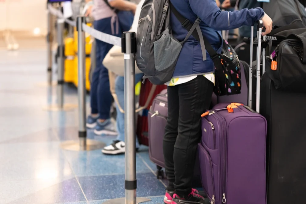 Travelers with purple suitcases and backpacks waiting in line at an airport check-in counter