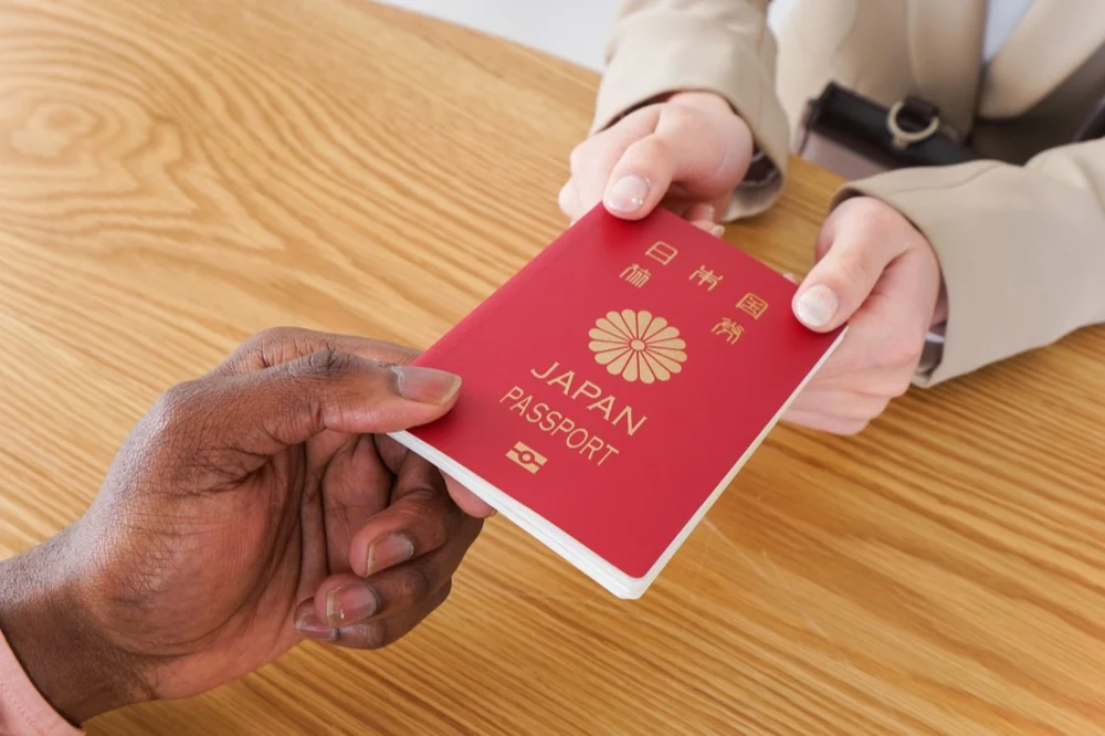 Two hands passing a red Japan passport across a wooden counter
