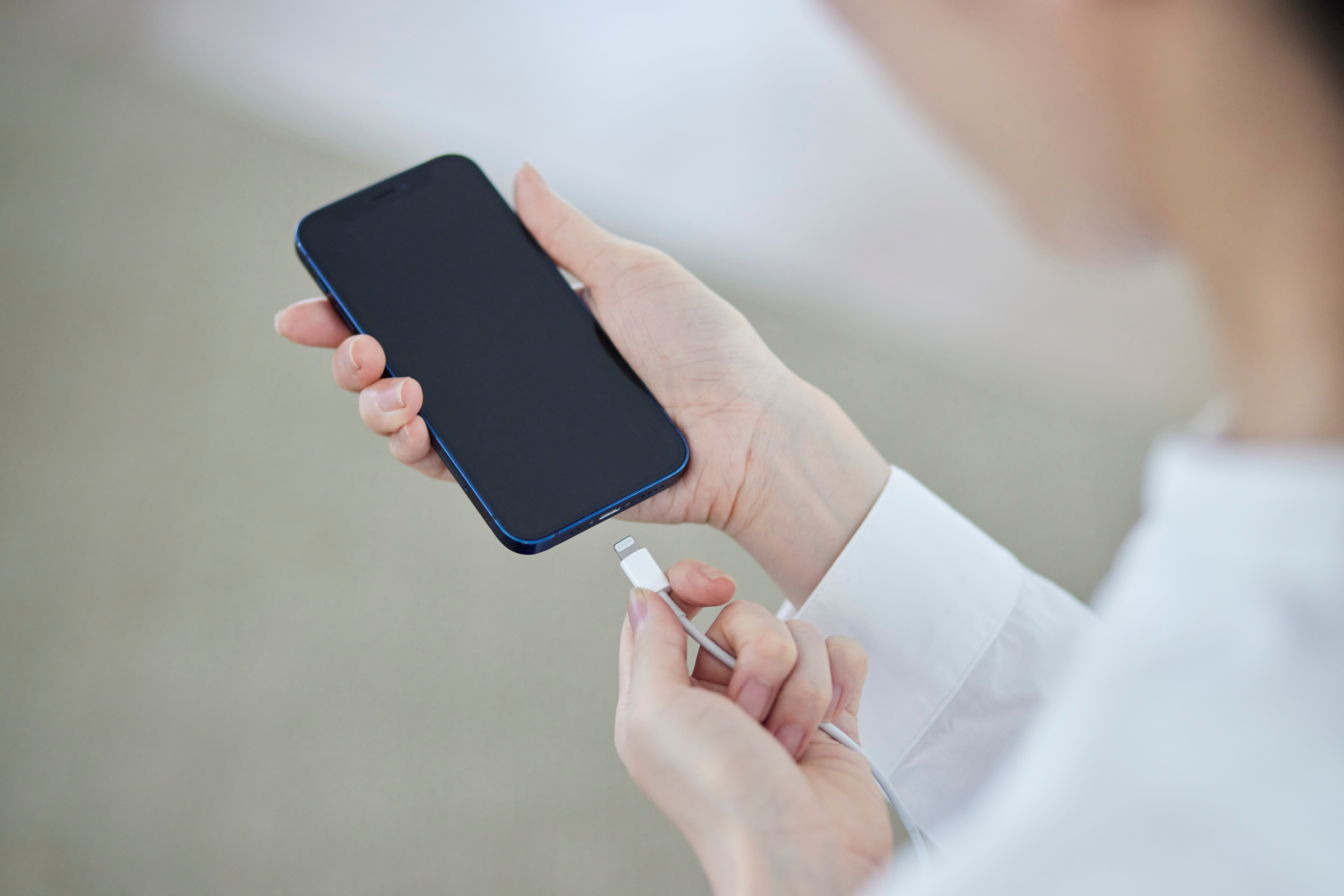 Close-up of hands holding a smartphone while connecting a Lightning charging cable