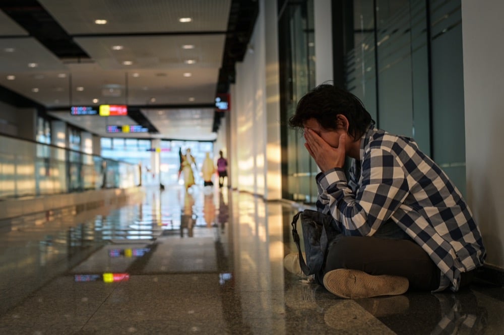 Distressed man sits on airport floor with head in hands