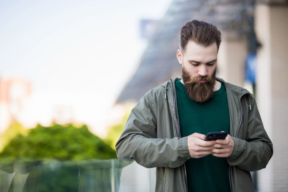 A bearded man using his smartphone while standing outdoors