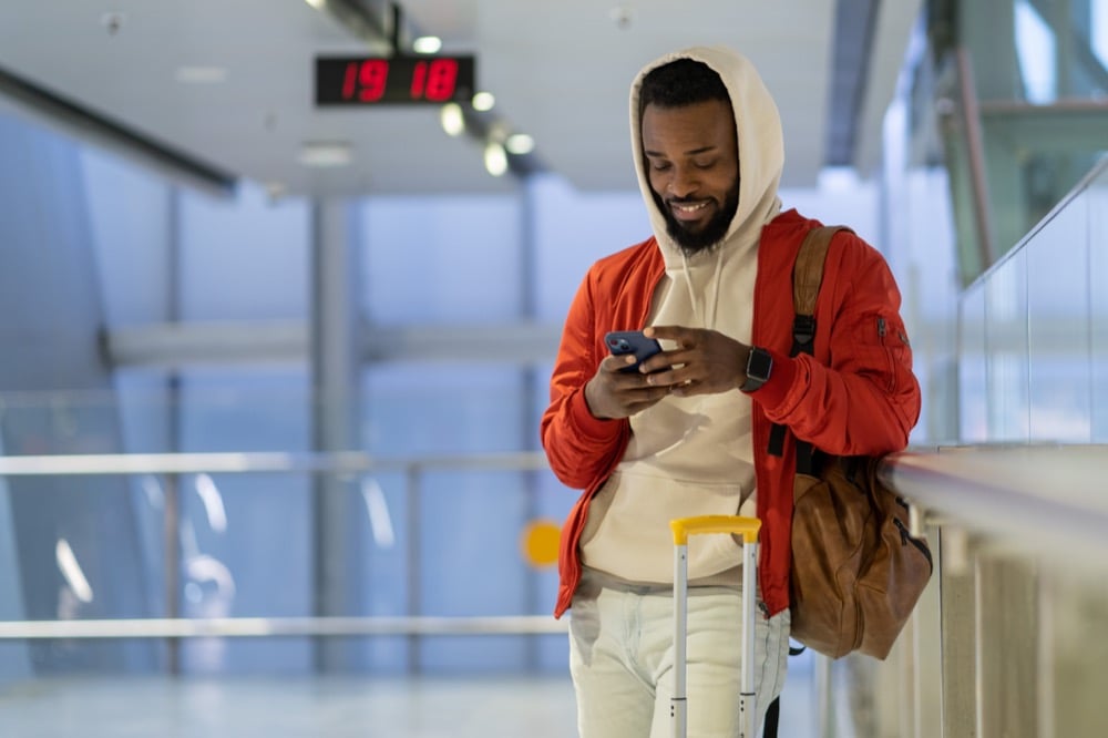 Smiling man with luggage using smartphone in an airport terminal