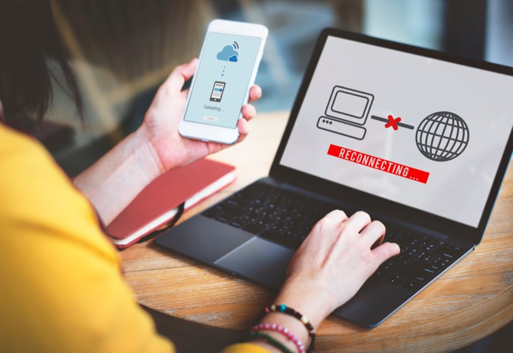 A person using laptop with　reconnecting message and smartphone on table