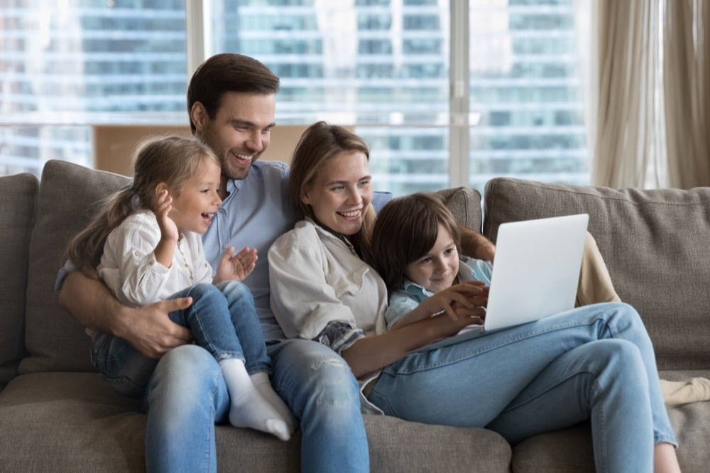 A happy family of four watching a laptop together on a sofa