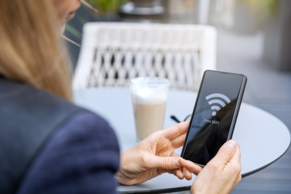 A person holding a smartphone displaying a free Wi-Fi screen at an outdoor cafe