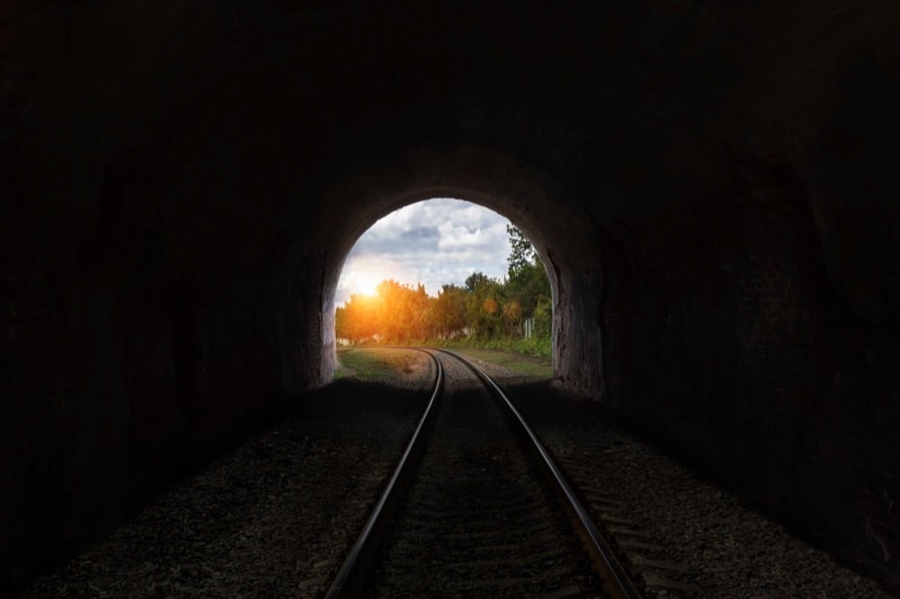 Railroad tracks inside a dark tunnel opening to sunlight, illustrating signal loss in tunnels