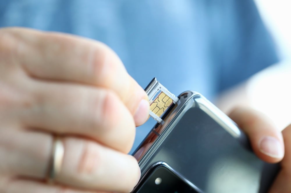 Hands inserting a physical SIM card into a smartphone tray