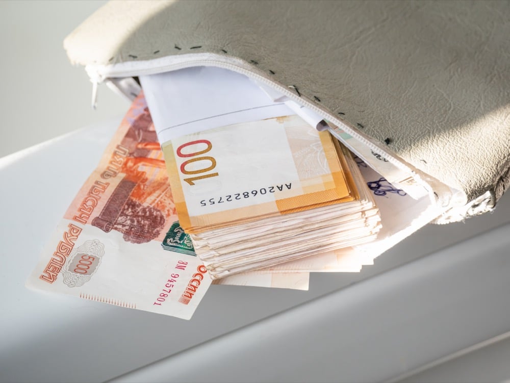 A stack of Russian ruble banknotes spilling out of an open white zipper pouch on a surface