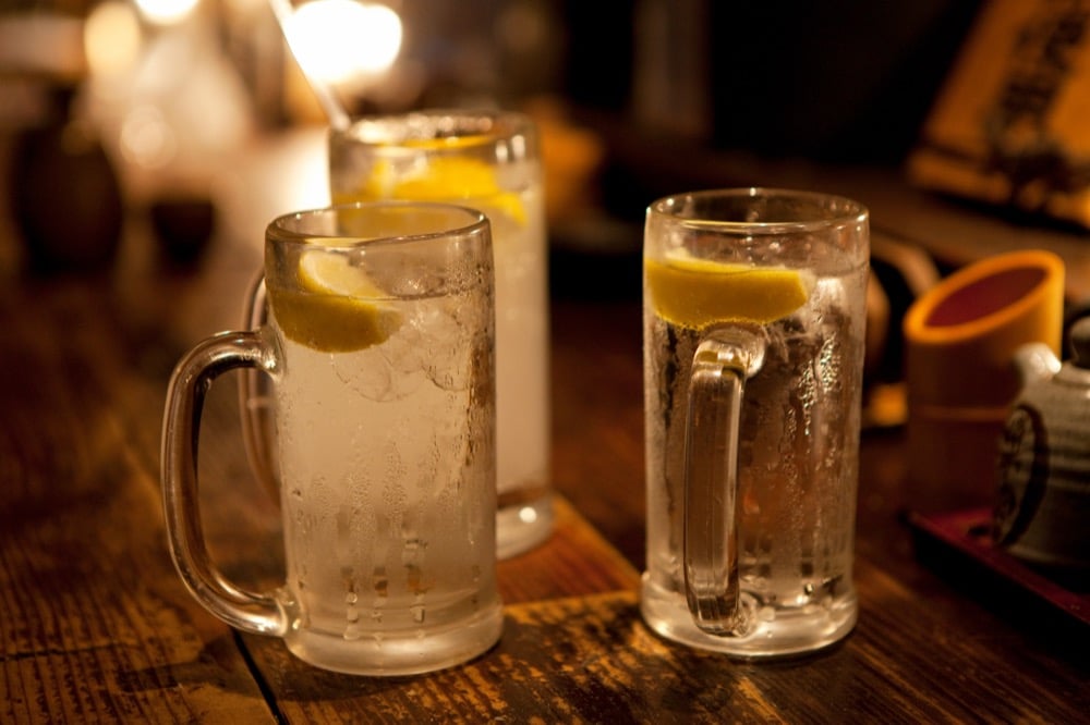 Three chilled lemon sour drinks served in glass mugs on a wooden table