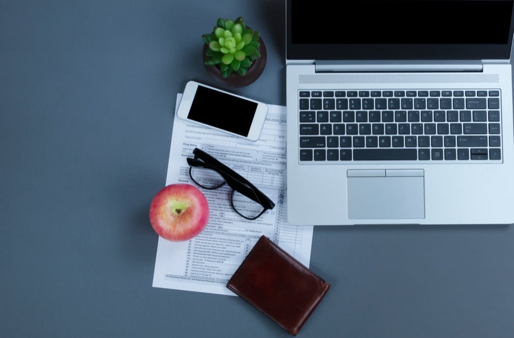 A laptop tax form smartphone glasses apple and wallet arranged on a desk