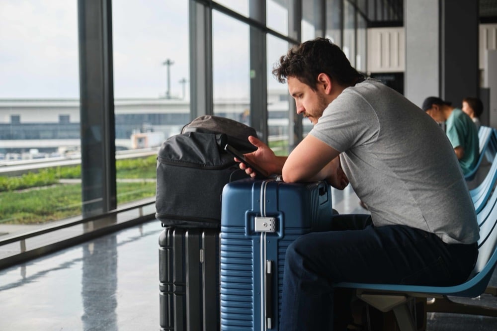 Man sitting with suitcases in an airport terminal looking at his smartphone