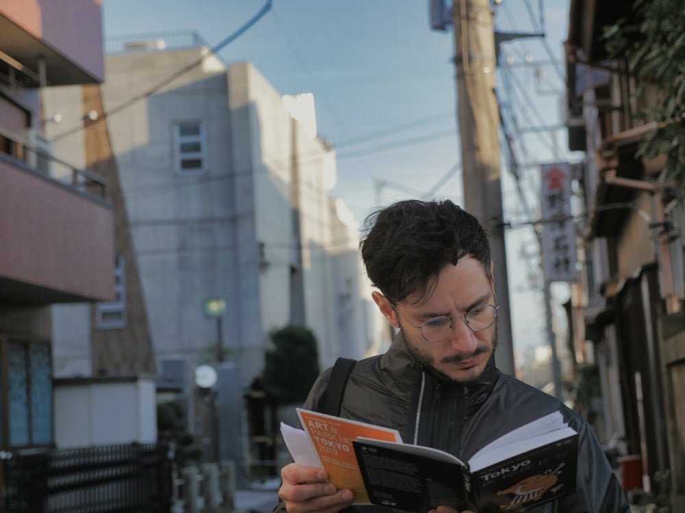 A man in glasses reading guidebook on an urban city street