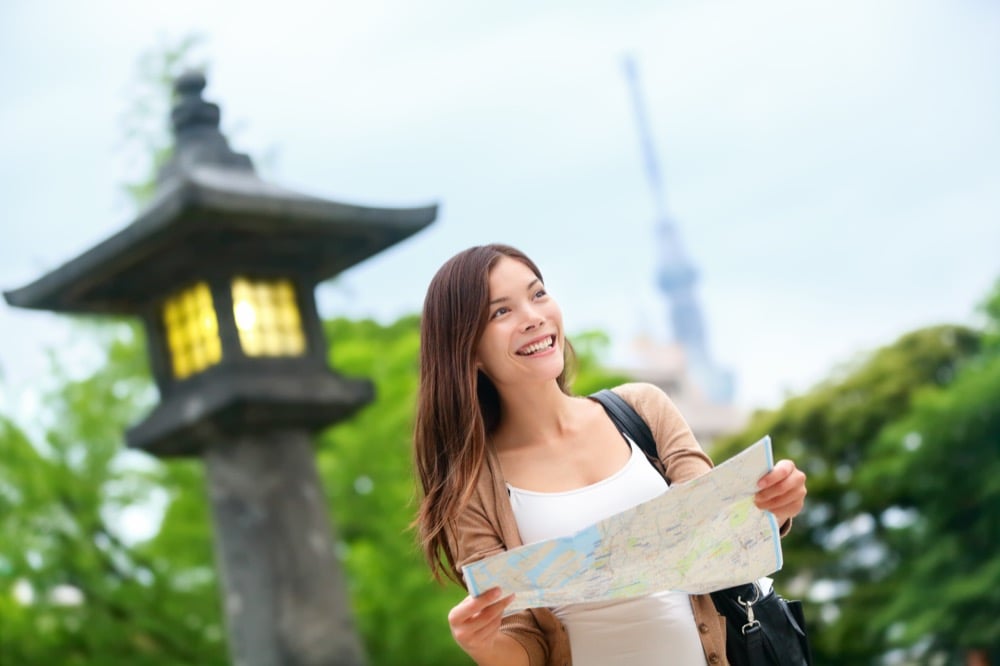 A smiling woman holding a map near a traditional stone lantern