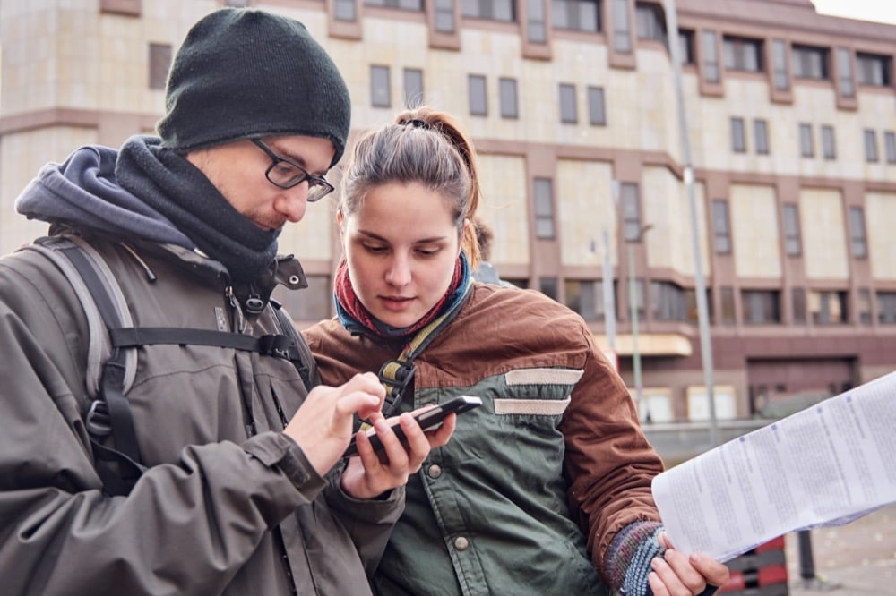 Two travelers check smartphone and map on a city street