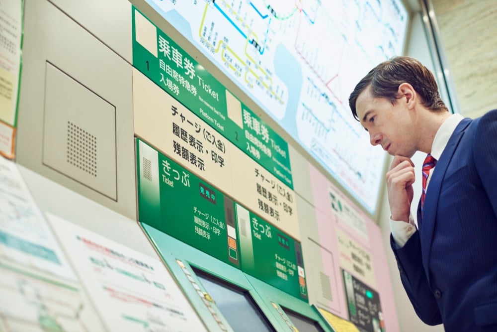 A man in suit thoughtfully examining a Japanese train ticket machine