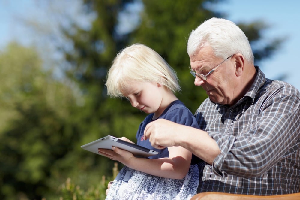 Elderly man and young girl sharing a tablet outdoors