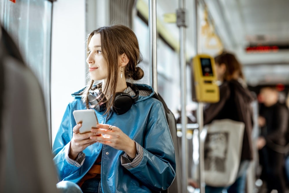 A woman holding a smartphone on a train, staying connected during her commute