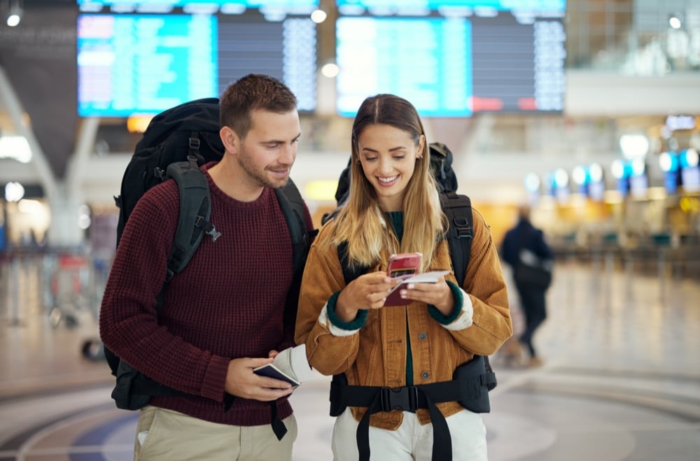 Two backpacker travelers checking their phones and passports at an airport departure hall