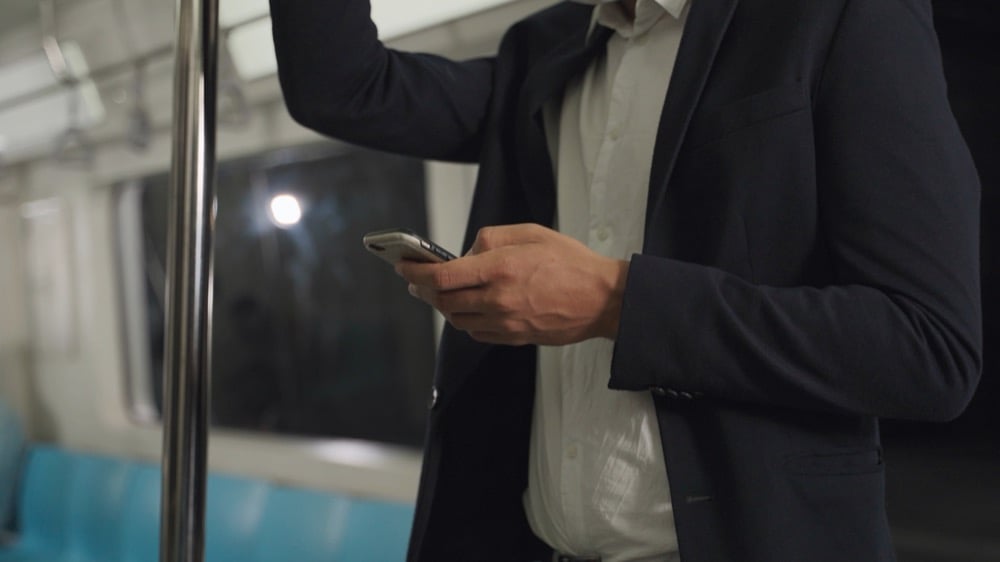 A man in a suit standing and using a smartphone on a train