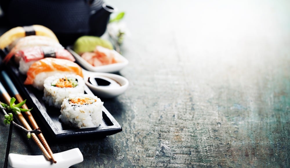Assorted Japanese sushi rolls and nigiri on a black plate with chopsticks and soy sauce dip