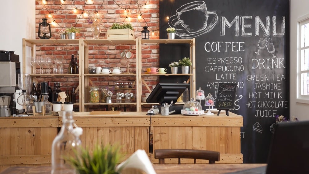 A cozy cafe interior with a wooden counter and chalkboard menu listing coffee drinks against a brick wall