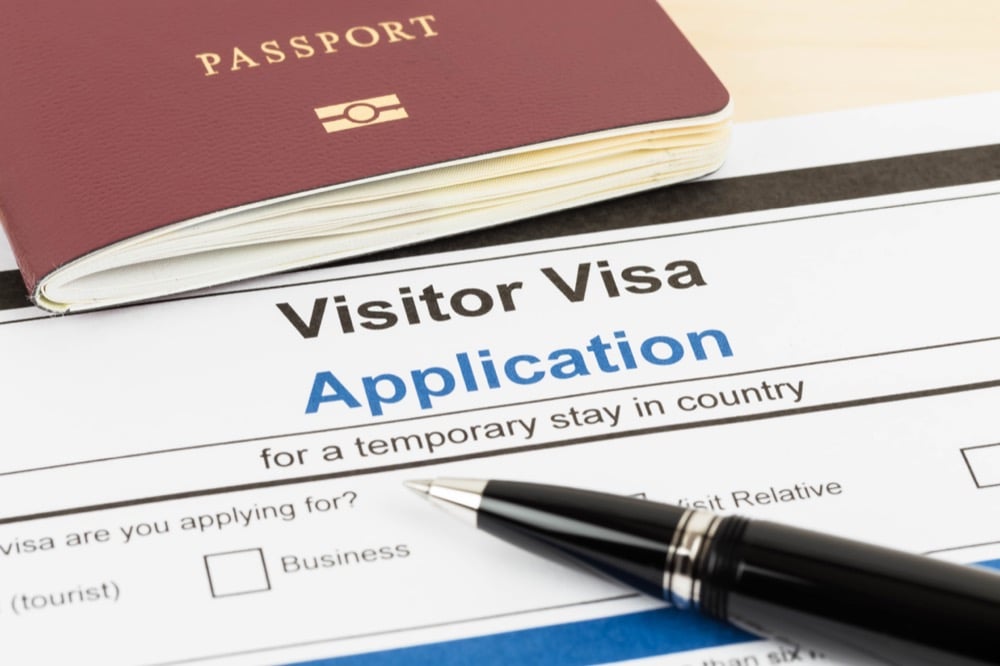 A visitor visa application form with a passport and pen placed on top