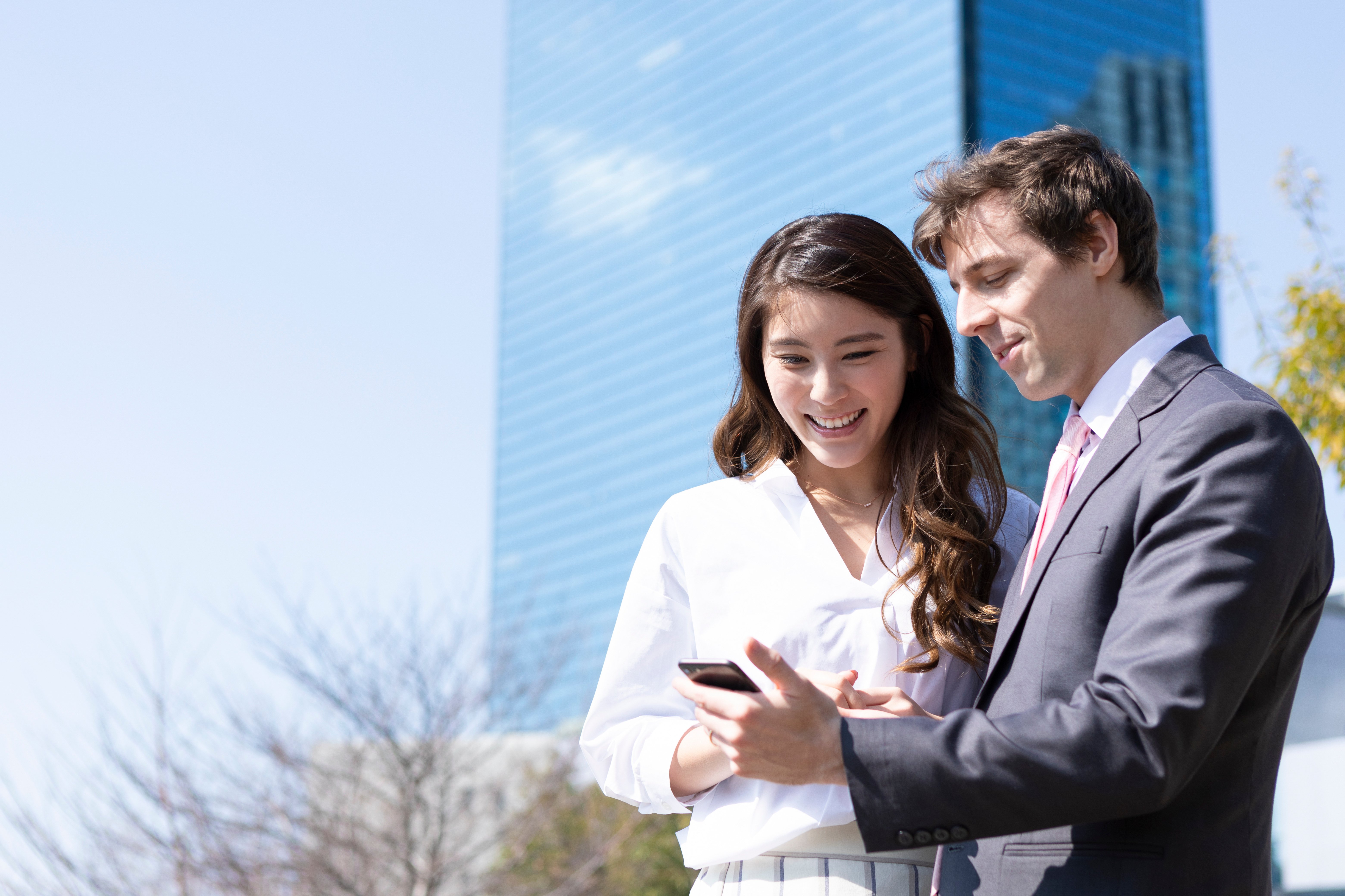Two business professionals outdoors smiling while looking at a smartphone together