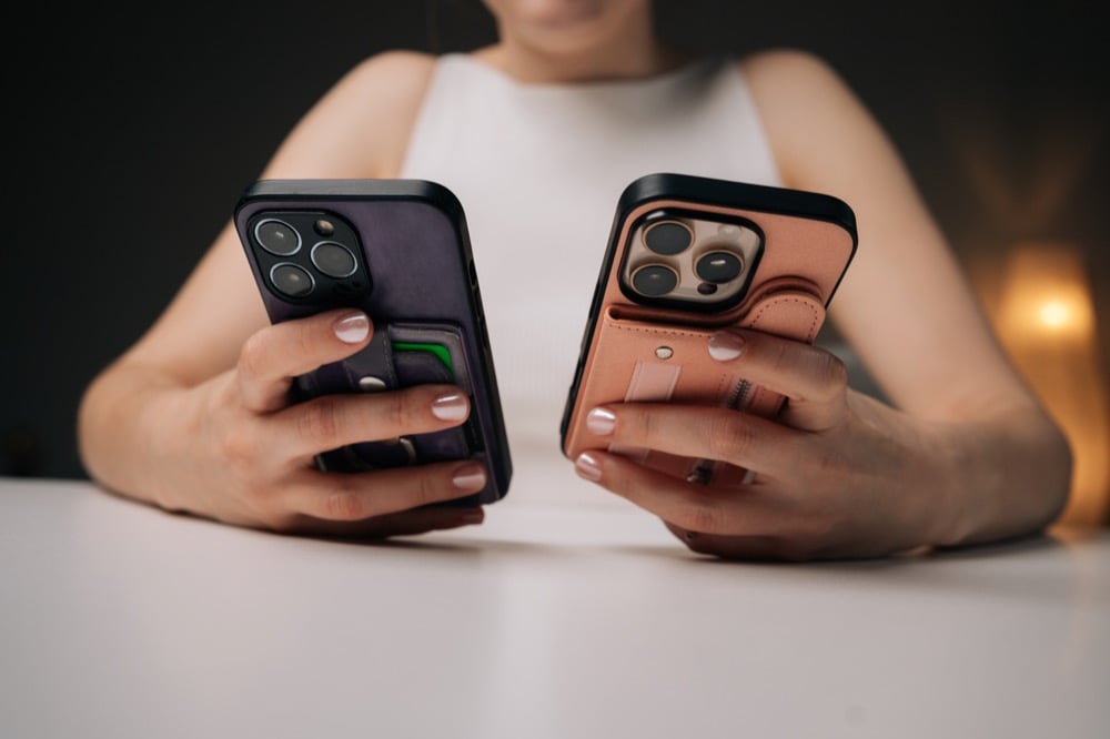 A person holding two smartphones with wallet cases side by side