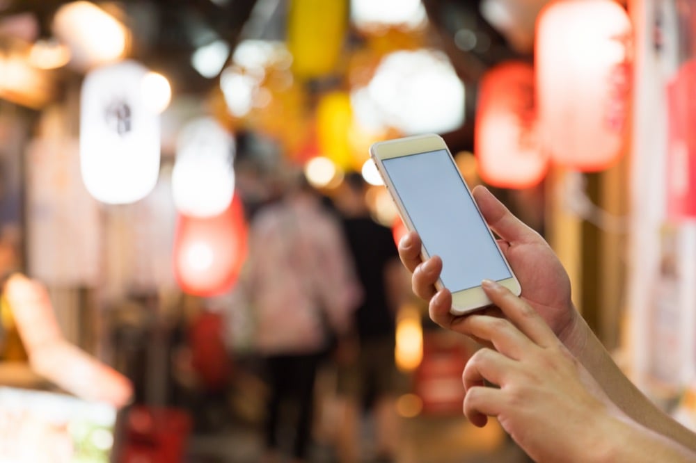 A person using a smartphone on a Japanese night street with lanterns and neon signs