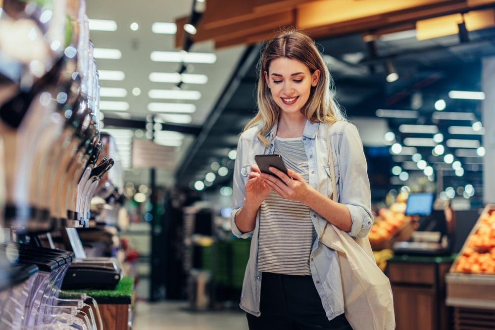 A smiling woman using a smartphone while shopping at a grocery store