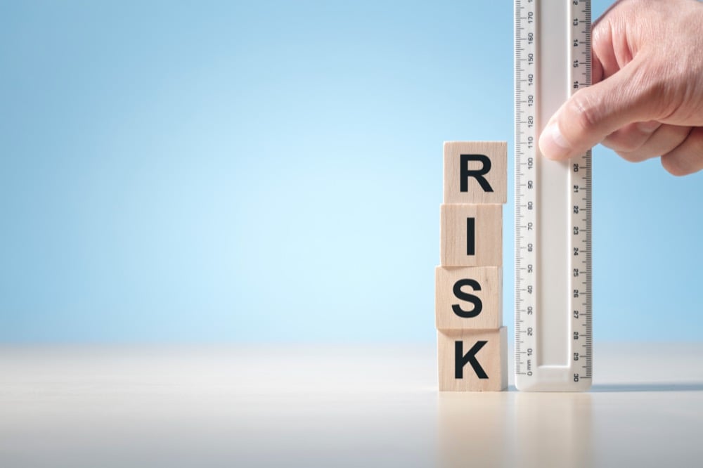 A hand measuring wooden blocks spelling RISK with a ruler against a blue background