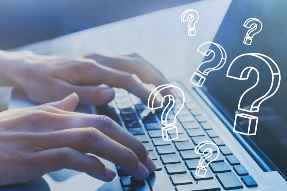 Hands typing on a laptop with floating 3D question marks