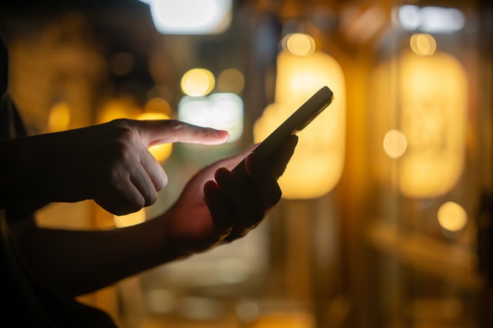 A close-up of a person's hands using a smartphone with warm city lights in the background