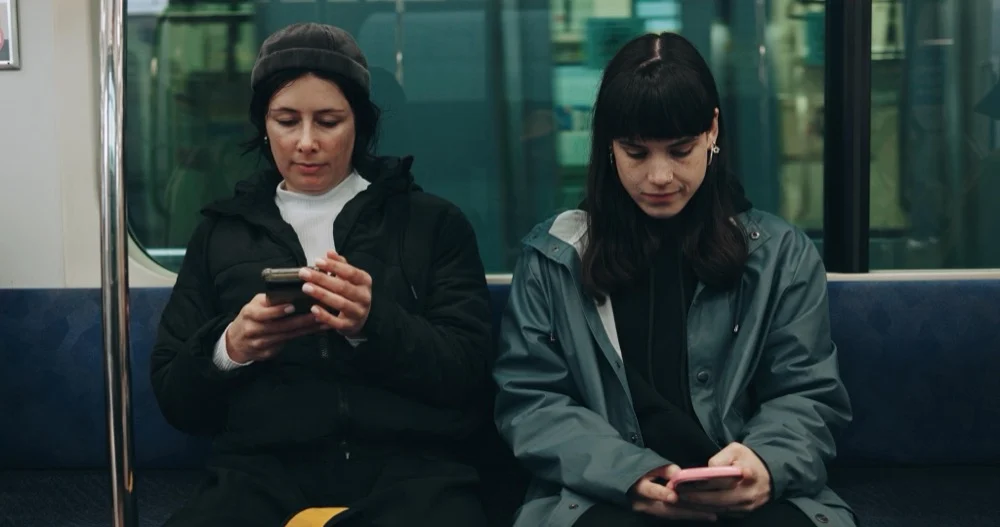Two women sitting on a train and looking down at their smartphones