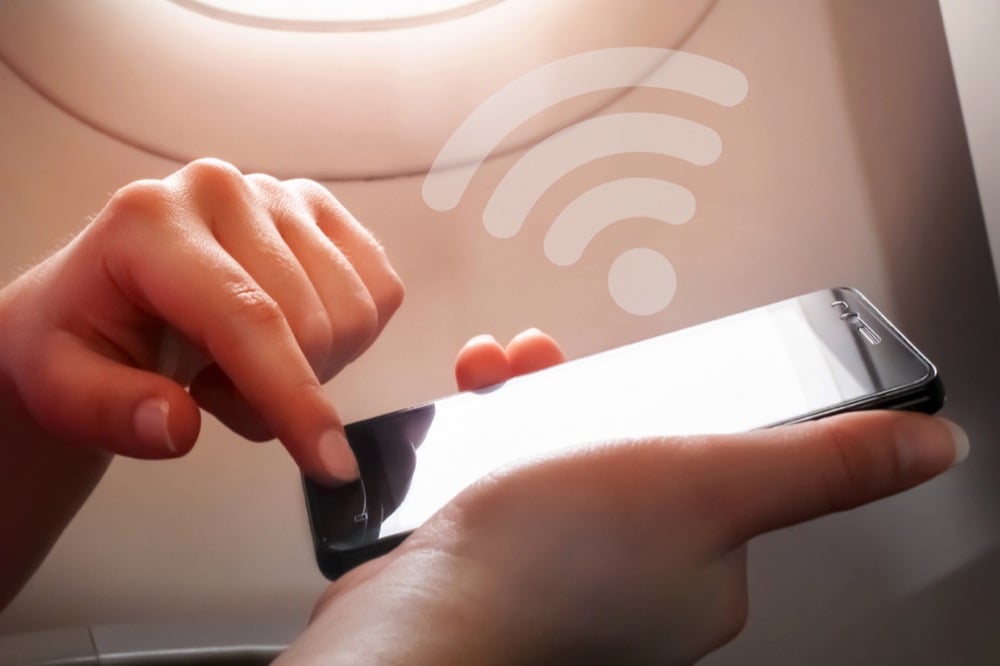 Hands on a phone near an airplane window with Wi-Fi icon