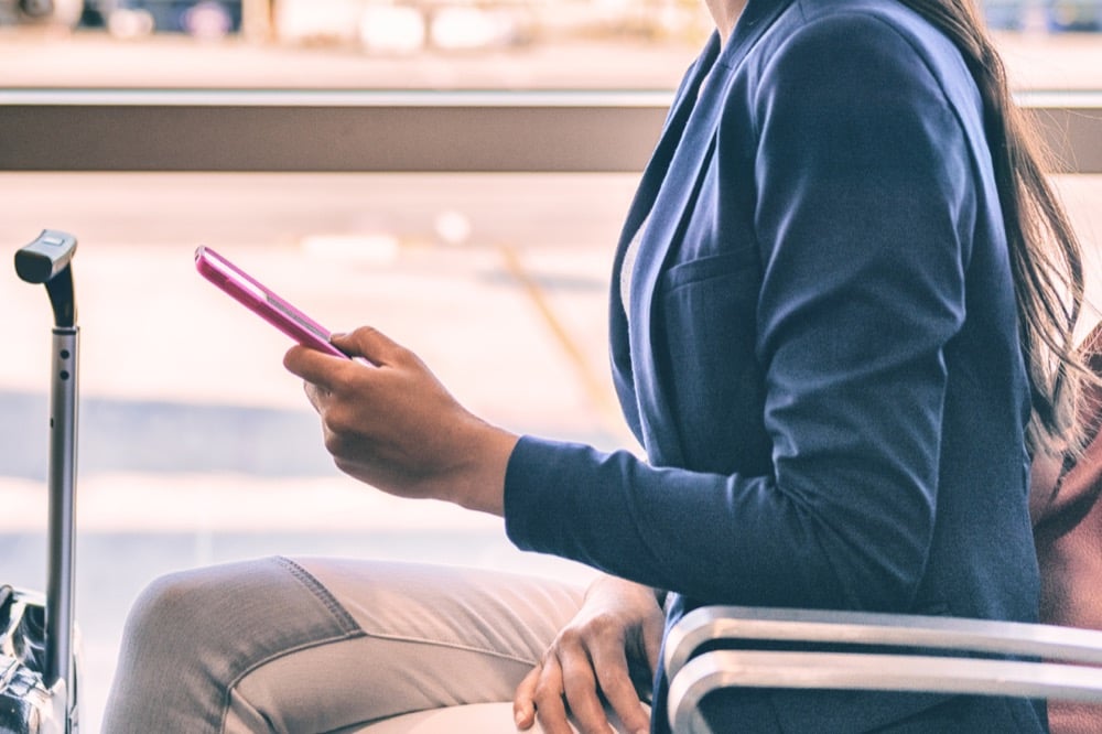 A businesswoman sitting at an airport terminal and using a pink smartphone