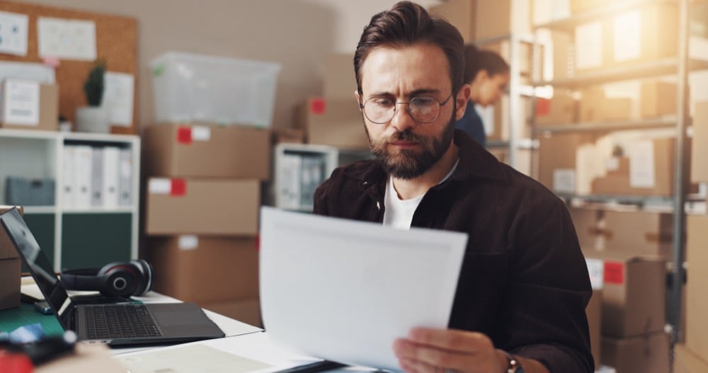 Bearded man with glasses reviewing documents at warehouse office desk