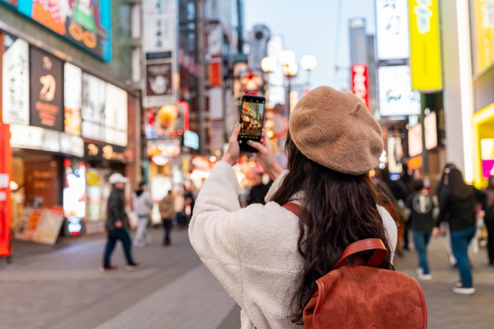 Tourist photographing Dotonbori's neon-lit street at night