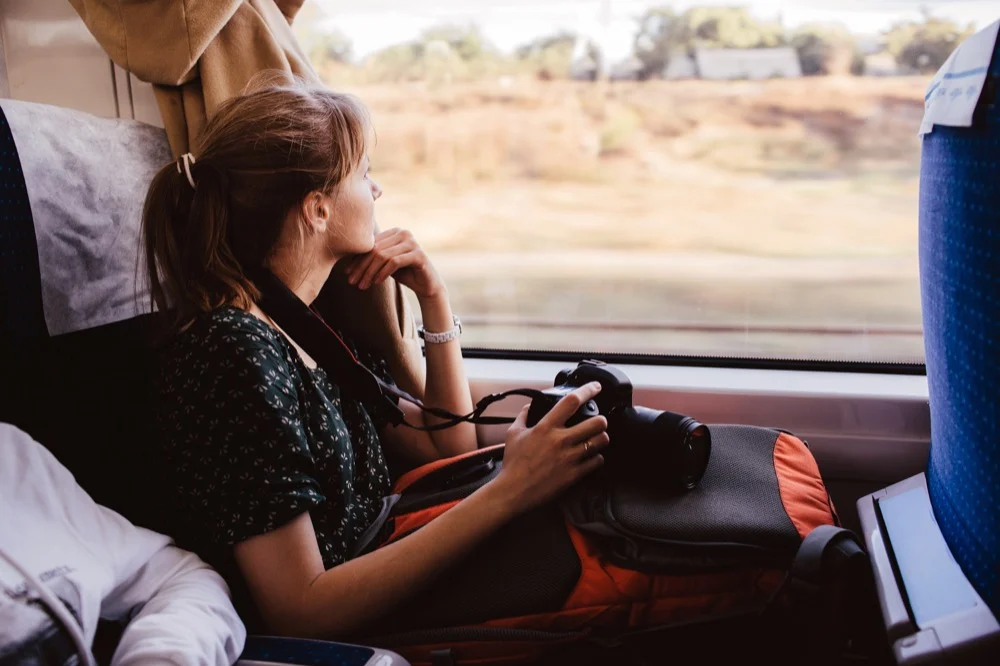 A female traveler holding a camera gazing out the window while riding a train through countryside