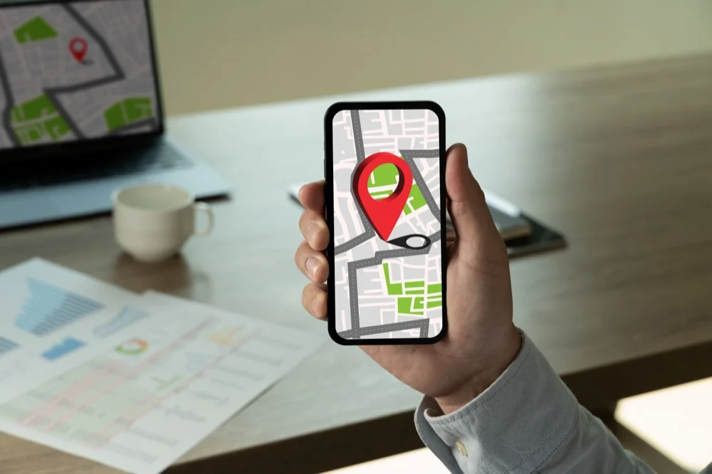 A hand holding a smartphone displaying a GPS map navigation app with a red location pin