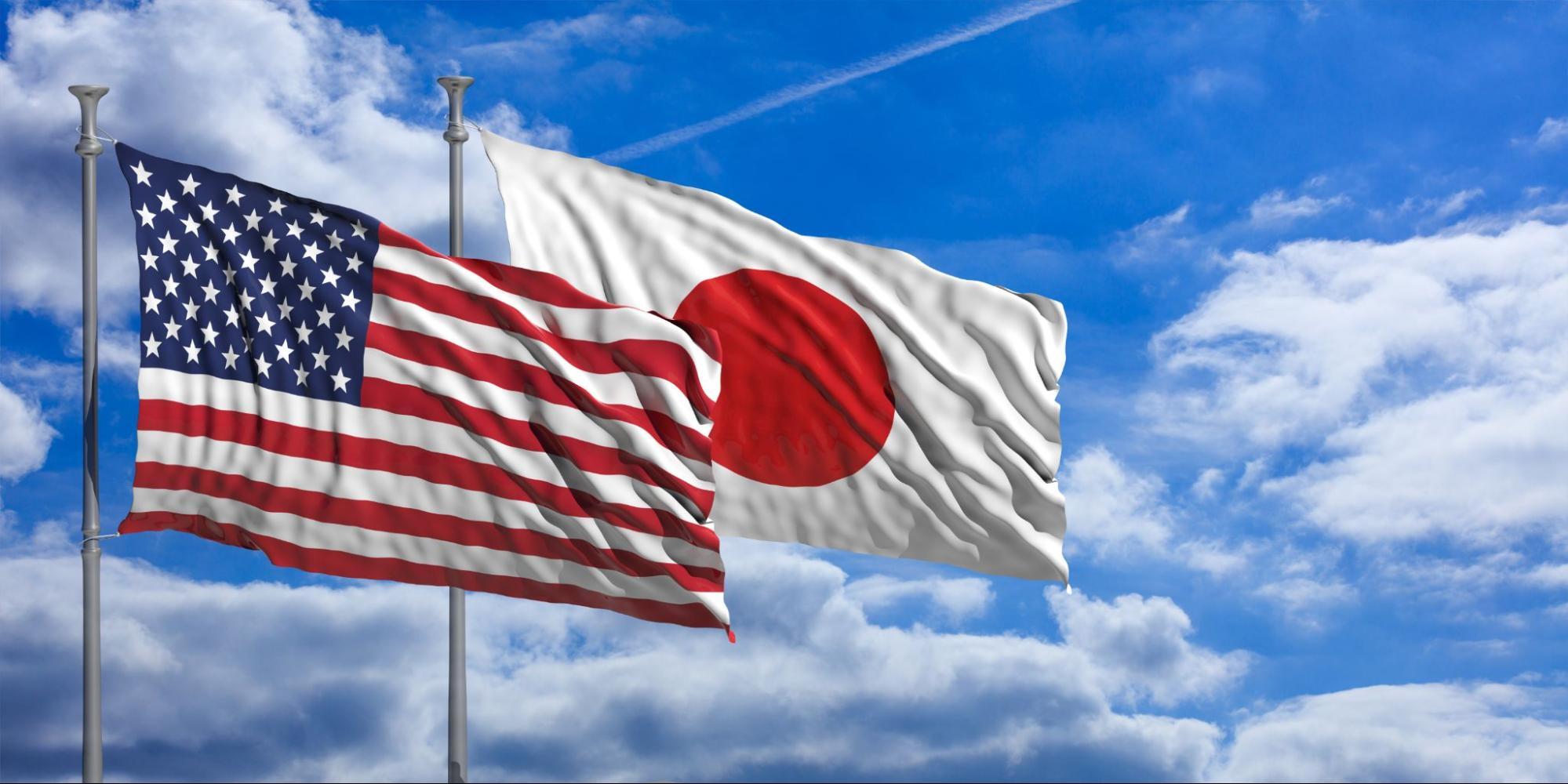 American and Japanese flags waving side by side against a blue sky