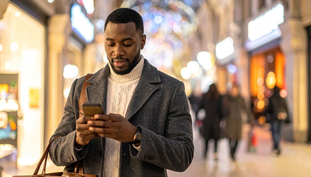 A man walks through an arcade at night, looking at his smartphone