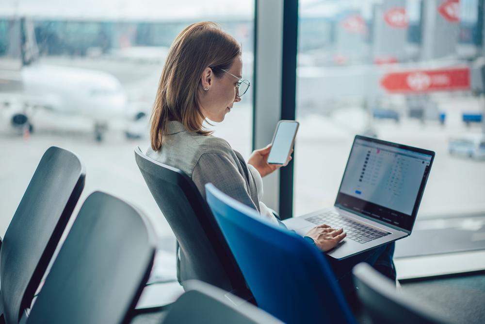 A woman is working on her laptop and checking her smartphone