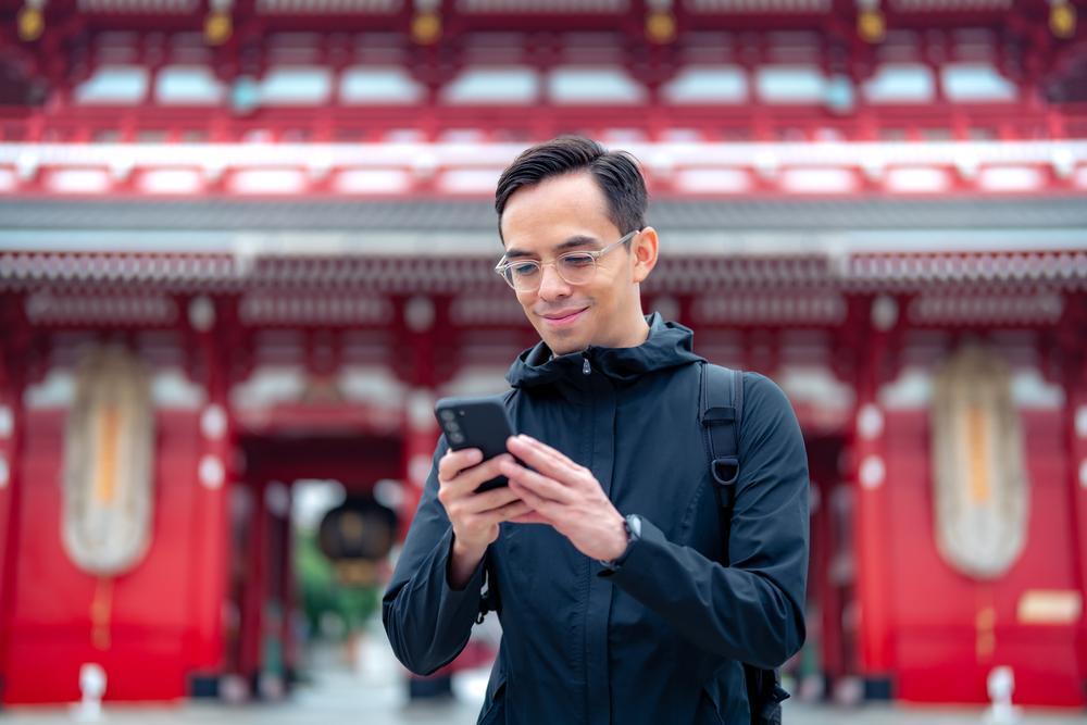 A man is looking at his smartphone in front of a Japanese temple